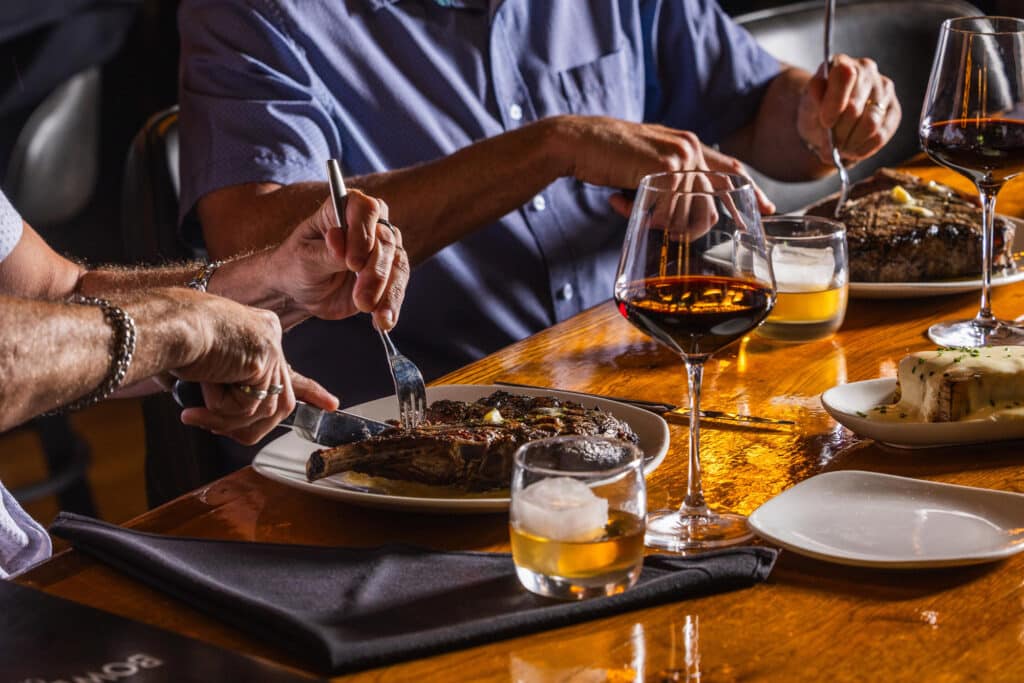 Two men cutting into steaks at the Bowdie's Chophouse bar in HHI, SC.