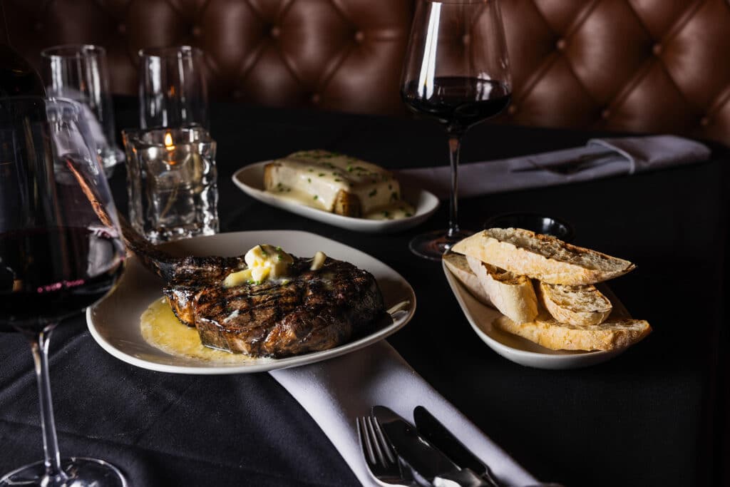 A steak, au gratin potatoes, and bread being served on a table at Bowdie's Chophouse