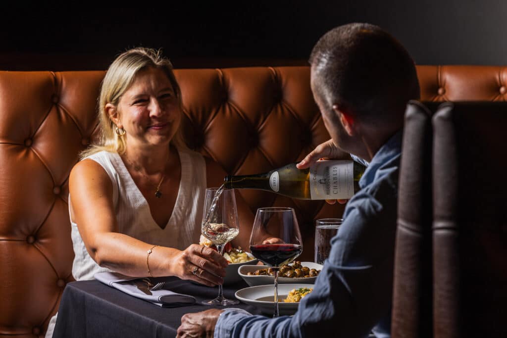 A man pours his wife a glass of white wine while dining at Bowdie's Chophouse in Hilton Head, SC, for Valentine's Day.